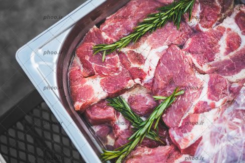عکس گوشت داخل ظرف فلزی و سبزی روی آن