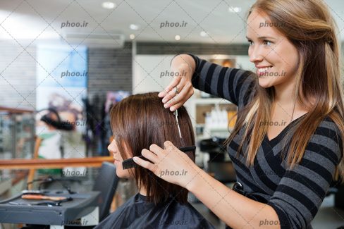 عکس آرایشگر با لبخند در حال اصلاح مو های خانم مشتری در آرایشگاه