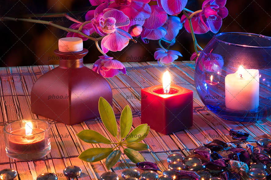 عکس برگ ، شمع ، روغن ، عطر ، گل و ظرف شیشه ای روی میز