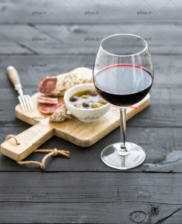 عکس جام شراب در کنار زیتون و ژامبون روی تخته چوبی
