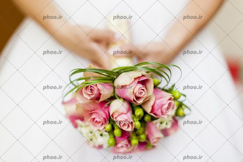 عکس با کیفیت یک دسته گل رز صورتی در دست عروس