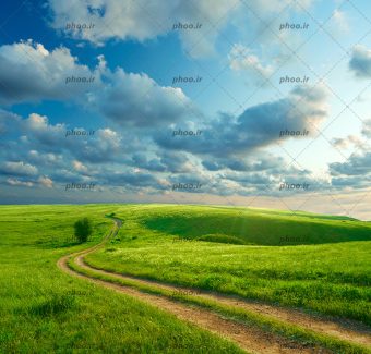 عکس با کیفیت جاده خاکی در دشت سبز با ابرهایی در آسمان آبی