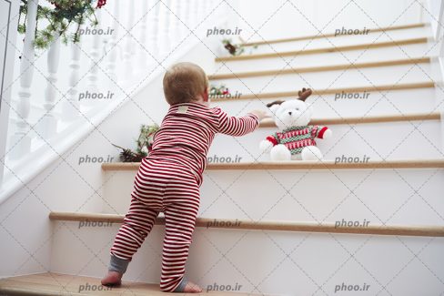 عکس کودک ایستاده در کنار پله ها در حال تلاش برای برداشتن عروسک