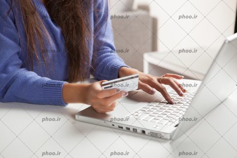 عکس با کیفیت خانم در حال کار با لپ تاپ و کارت اعتباری در دست