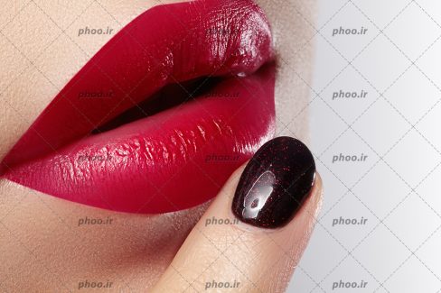 عکس لب های زن با آرایشی زیبا به رنگ قرمز و ناخن با مانیکور رنگ تیره روی لب
