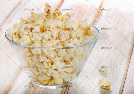 عکس کاسه شیشه ای از پاپکورن در پس زمینه چوبی
