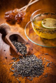 عکس چای خشک سبز ریخته شده روی میز و فنجان چای