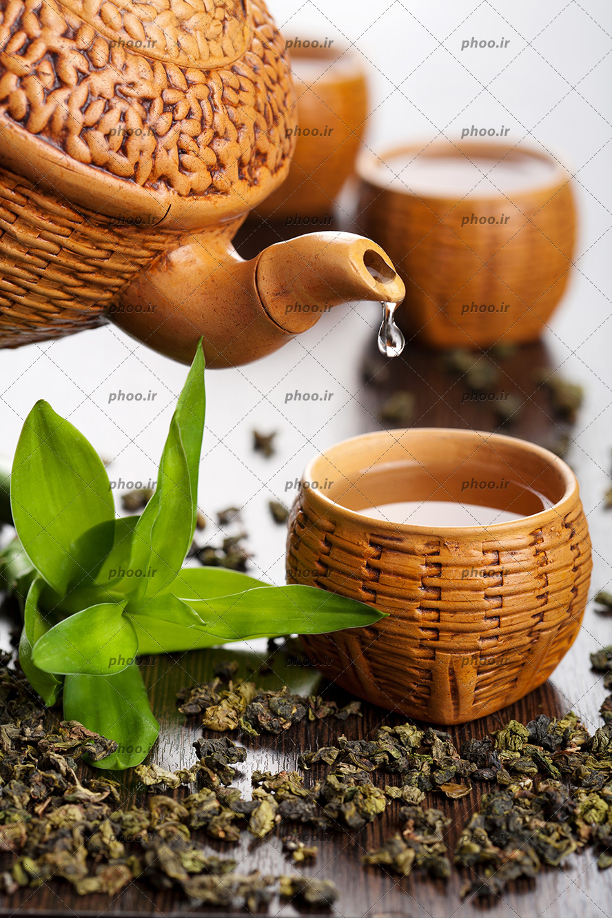 عکس قوری سفالی درحال ریختن آبجوش در لیوان های چای سفالی