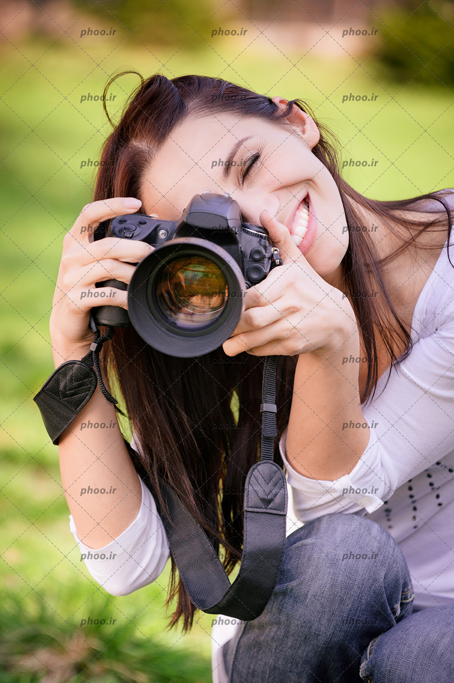 عکس با کیفیت خانم با لبخند در حال عکاسی با دوربین در پس زمینه محو سبز