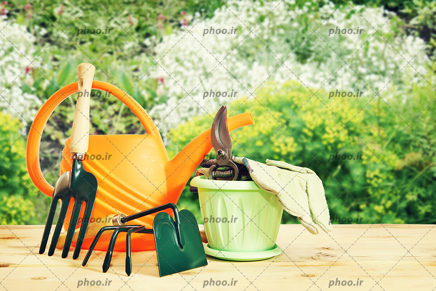 عکس ابزار باغبانی روی میز چوبی در پس زمینه باغ سر سبز