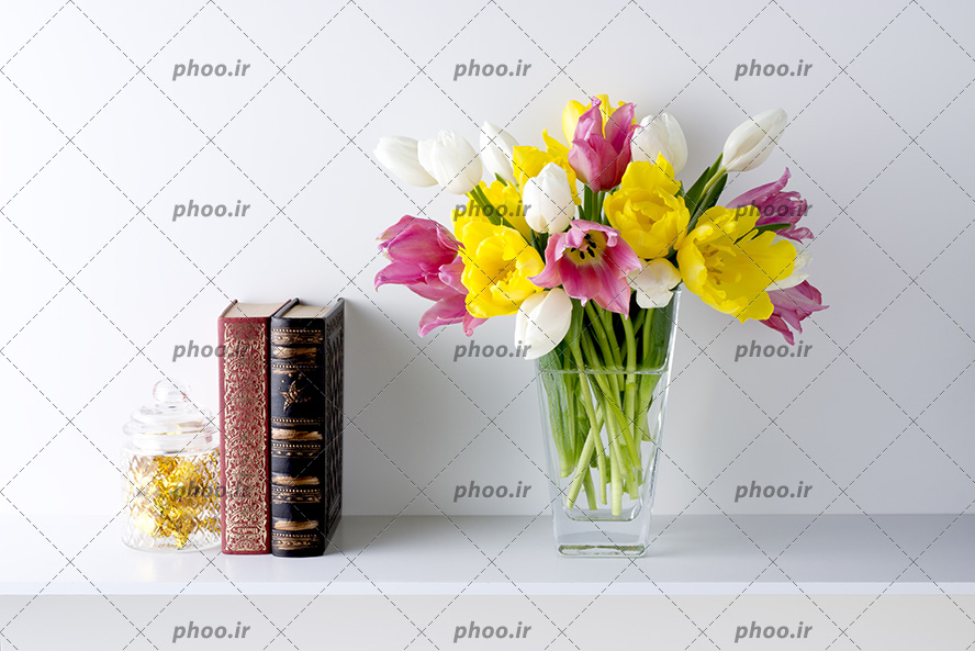عکس گلدان شیشه ای با گل های زیبا در کنار دو کتاب روی میز