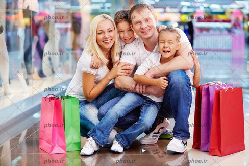 عکس با کیفیت یک خانواده چهار نفره با کیسه های خرید اطراف آن ها در فروشگاه