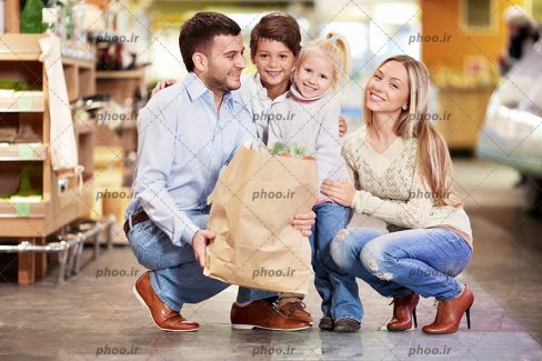 عکس با کیفیت یک خانواده چهار نفره شاد با یک کیسه ی خرید در فروشگاه