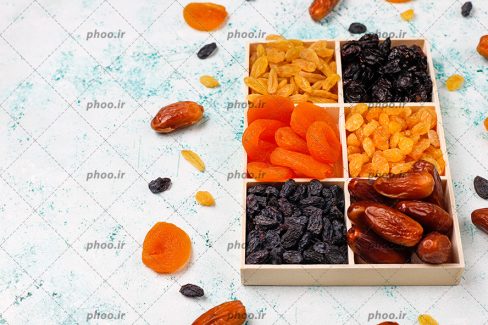 عکس با کیفیت اردو خوری پر شده از خشکبار خوشمزه و مفید و چند خرما و کشمش و مویز و زردآلود در اطراف ظرف