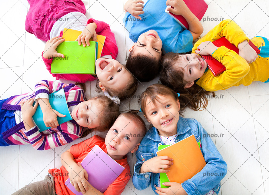 عکس با کیفیت دختر بچه و پسر بچه های خوابیده در کنار یکدیگر در حال خندیدن و گرفتن کتاب های خود در بغل