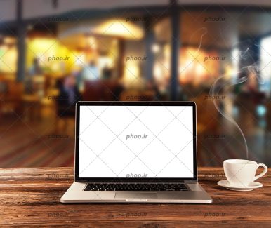 عکس لپ تاپ در کنار یک فنجان نوشیدنی داغ روی میز چوبی