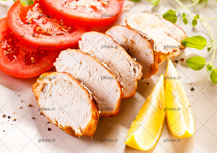 عکس برش هایی از گوشت در کنار گوجه و لیمو در پس زمینه سفید