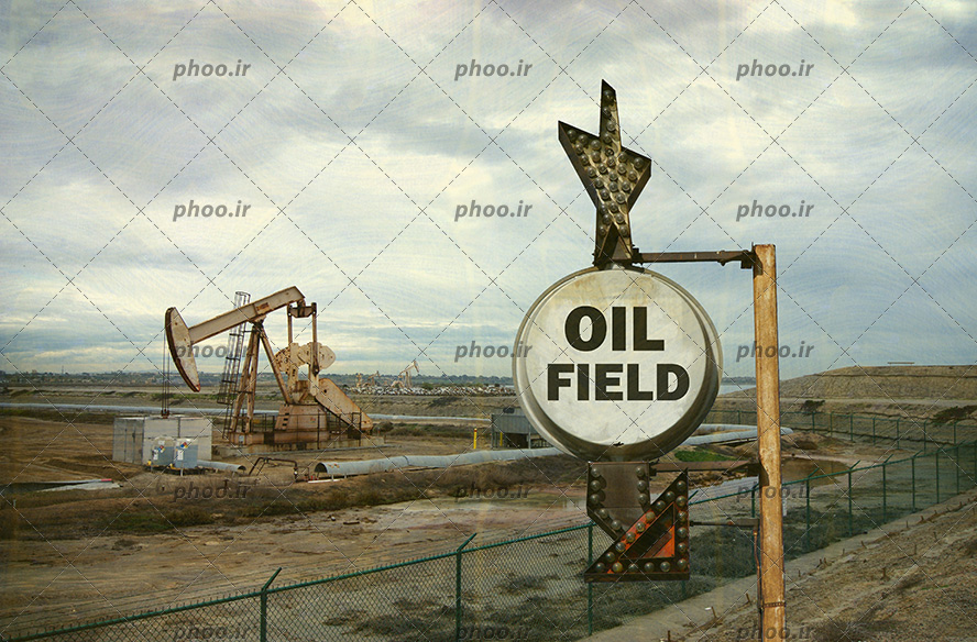 عکس یک تابلو با نوشته انگلیسی (oil field) به معنی حوزه های نفتی برای نشان دادن مسیر در پس زمینه پمپ نفت