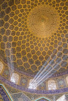 عکس نمای داخلی مسجد با گنبد کاشی کاری شده زیبا با آیات قرآن و پنجره های چوبی که از آن نور به زیبایی در جهت های مختلف به داخل تابیده شده