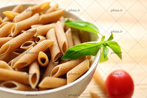 عکس پاستا در کاسه و یک گوجه روی زمین از نمای نزدیک