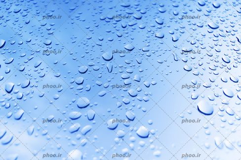 عکس قطره های آب بر روی شیشه در پس زمینه آبی