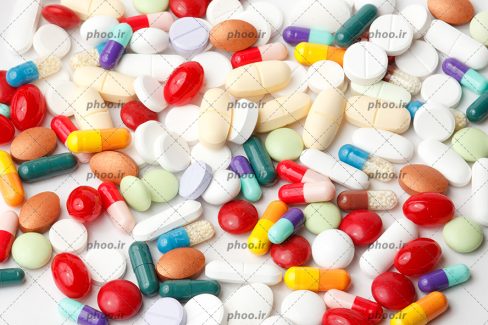 عکس مجموعه ای از قرص ها و کپسول های دارویی با رنگ های مختلف در پس زمینه سفید