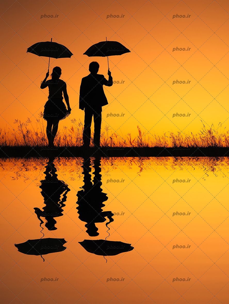 عکس با کیفیت زن و مرد جوان با چتر در دست در کنار دریاچه در مقابل غروب خورشید