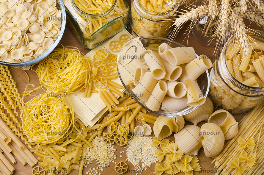 عکس ماکارونی های خام ریز و درشت ساده و فرمی در ظرف شیشه ای و روی زمین از نمای بالا