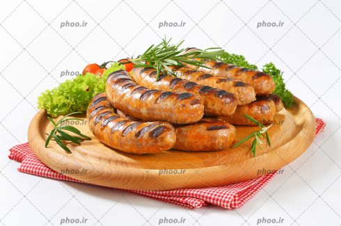 عکس سوسیس های کباب شده و سبزی روی تخته چوبی در پس زمینه سفید