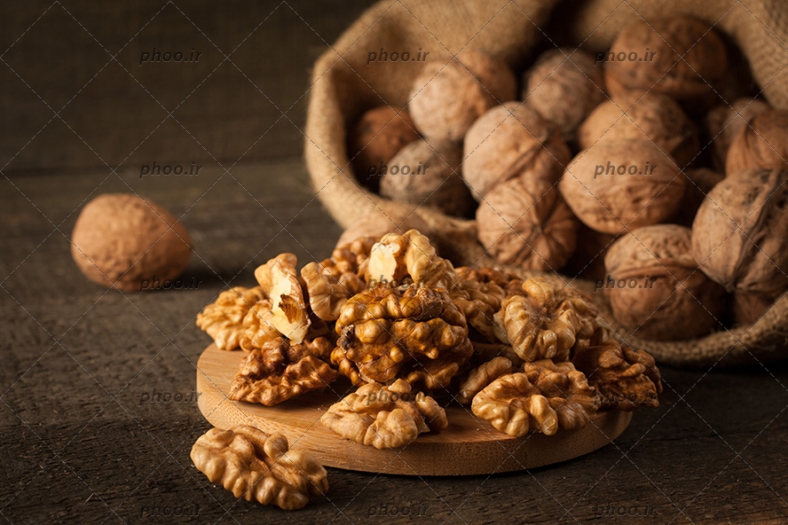 عکس گردو هایی در گونی کنفی و مغز گردو روی تخته چوبی