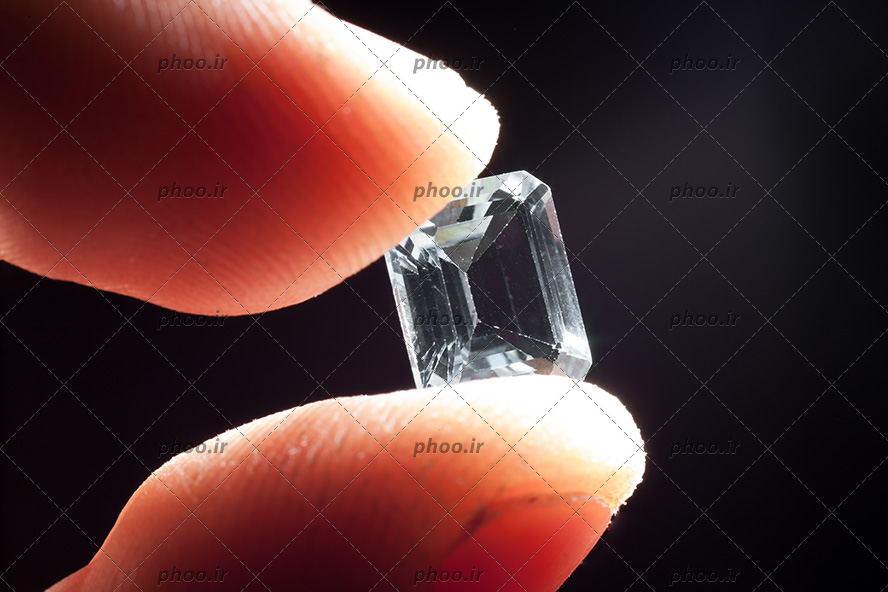 عکس سنگ قیمتی سفید براق بین دو انگشت در پس زمینه مشکی