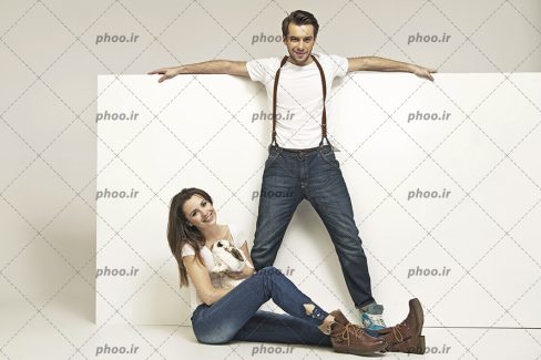 عکس با کیفیت زوج جوان شیک پوش با ژست جلوی یک تابلوی سفید بزرگ