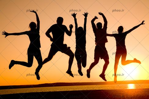عکس با کیفیت مردم شاد در حال پریدن در هوا در مقابل غروب خورشید