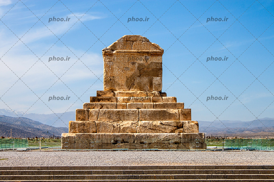 عکس یک مکان که از سنگ ساخته شده است و پله های سنگی و حصار ی که دور آن کشیده شده و آسمانی نیمه ابری