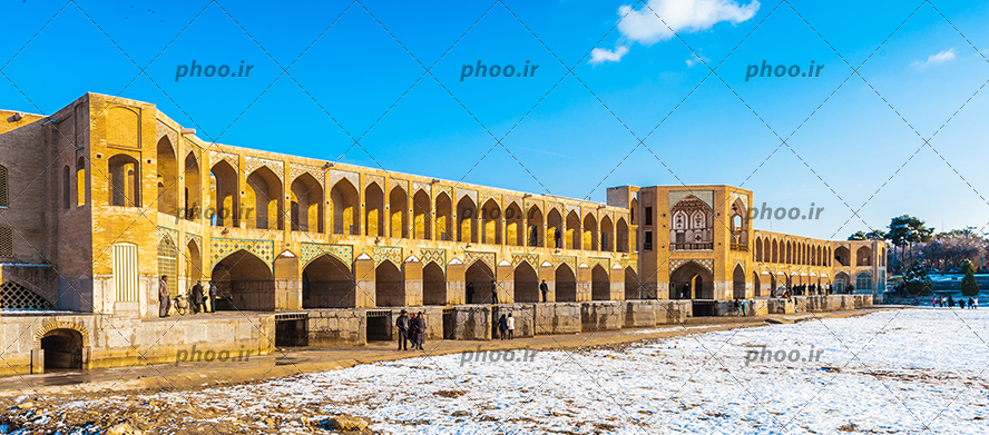 عکس یک پل با معماری جالب و طرحی متقارن بر روی رودخانه و مردمی که برای بازدید آمده اند