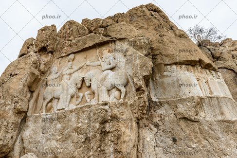 عکس نقش برجسته روی سنگ که با تراش کاری ایجاد شده است از دو سرباز که سوار بر اسب هستند و شمشیر در دست دارند