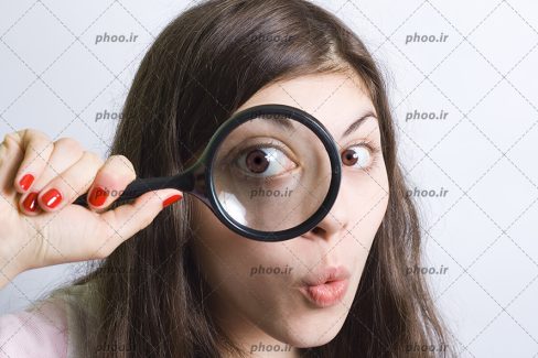 عکس با کیفیت دختر با تعجب در حال نگاه کردن از داخل ذره بین