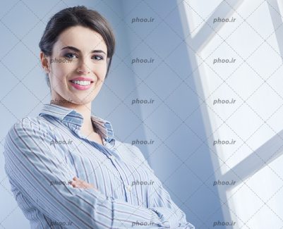 عکس خانم با لبخند و پیراهن راه راه آبی ایستاده در کنار پنجره