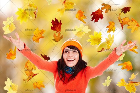عکس با کیفیت خانم شاد زیر بارانی از برگ های زیبای پاییزی