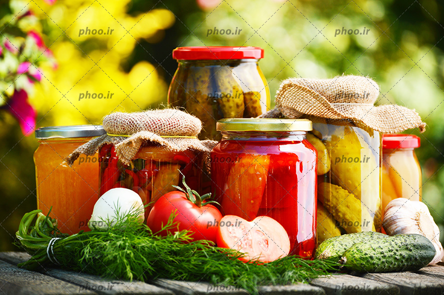 عکس ترشی های مختلف داخل ظروف سر بسته روی میز