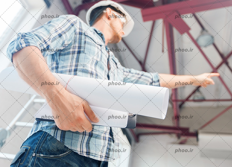عکس کارگر ساختمان با نقشه در دست و نشان دادن جهت با دست دیگر