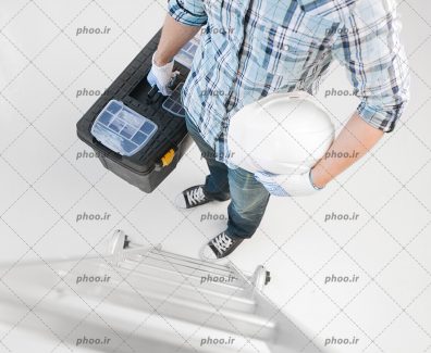 عکس کارگر با کلاه ایمنی و جعبه ابزار در دست کنار نردبان