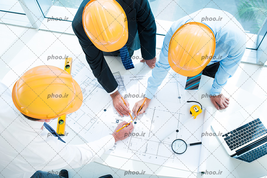 عکس سه مهندس با کلاه ایمنی مشغول طراحی و کار گروهی