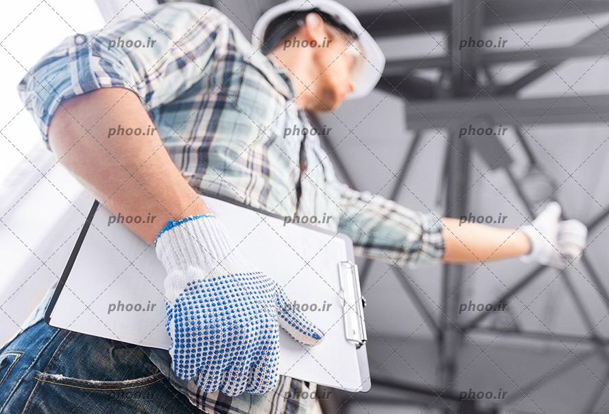 عکس مهندس ساختمان با کلاه ایمنی و طرح در دست و نشان دادن علامت لایک با دست