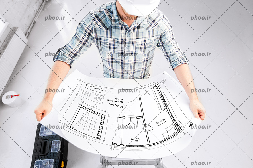 عکس مهندس ساختمان با کلاه ایمنی در حال بررسی نقشه