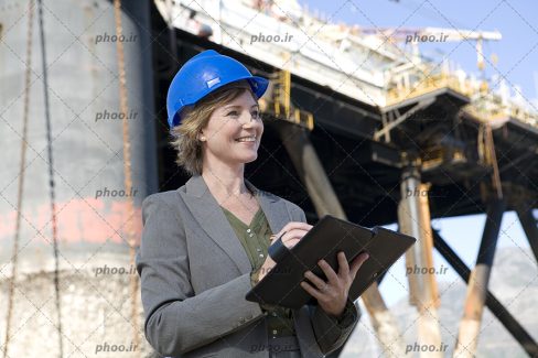 عکس مهندس خانم با لبخند و کلاه ایمنی ایستاده در کنار پل در حال ساخت