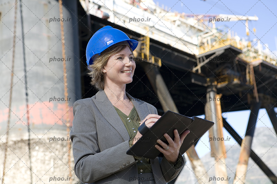 عکس مهندس خانم با لبخند و کلاه ایمنی ایستاده در کنار پل در حال ساخت