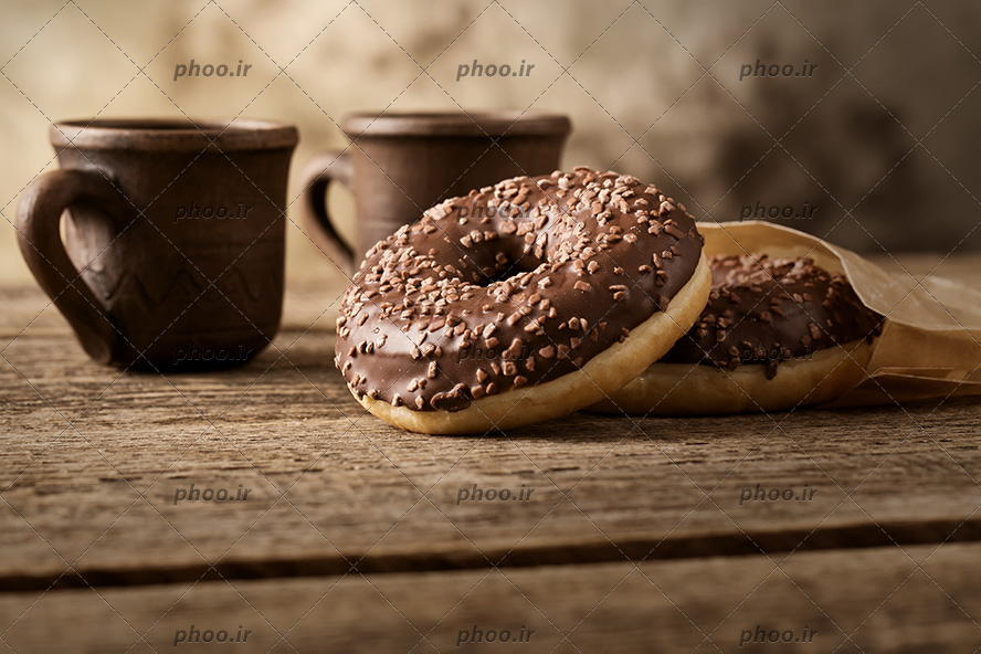 عکس دو عدد دونات با تزئین شکلات و دو فنجان نوشیدنی