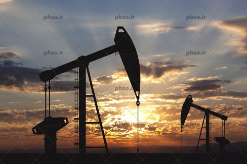 عکس پمپ روغن و نفت و کار در یک میدان نفتی در برابر غروب خورشید