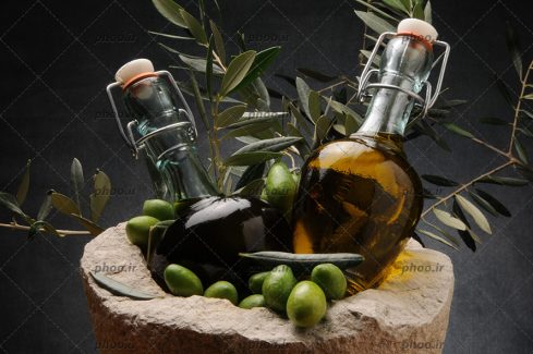 عکس با کیفیت بطری های شیشه ای از روغن زیتون در کنار زیتون در پس زمینه خاکستری